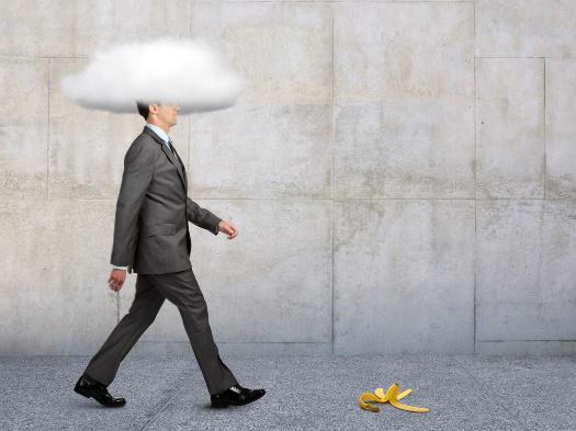 Man in suit with head in cloud walking toward a banana peel.