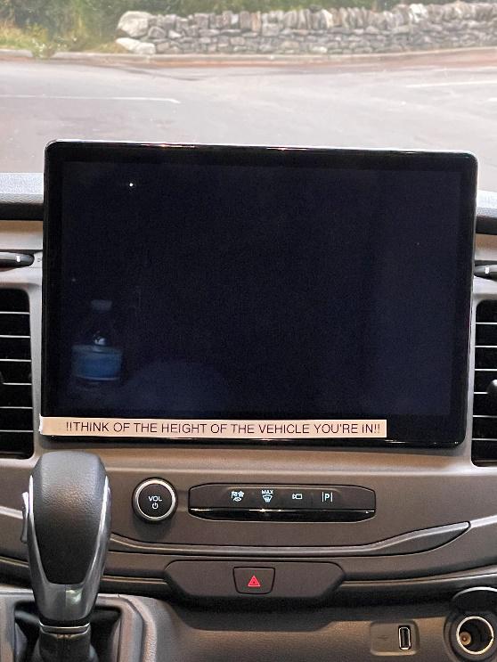 An inactive screen in a vehicle with a label on it that reads, '!!THINK OF THE HEIGHT OF THE VEHICLE!!'