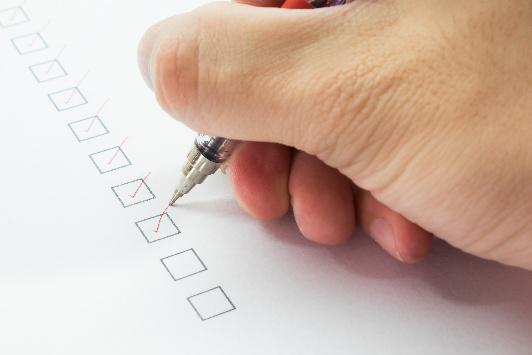 Hand holding a pencil checking a box in a list.