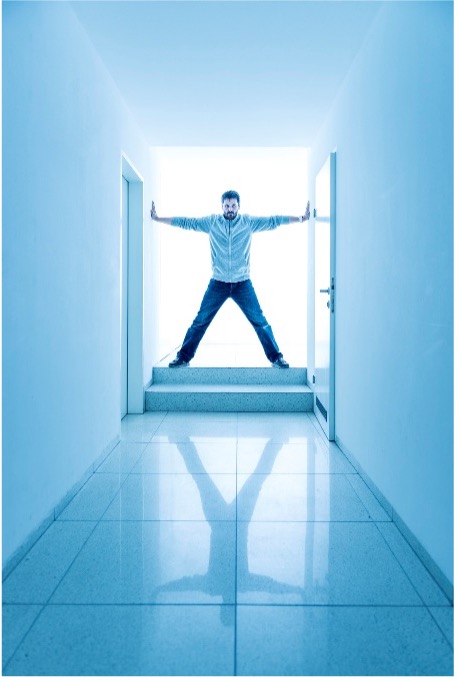 Backlit man in doorway of a blue room, doing a Vetruvian man pose, wearing all blue 