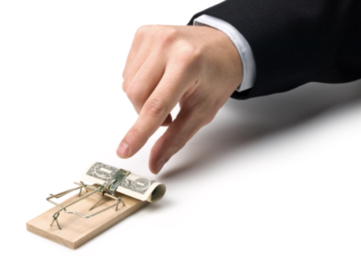 Hand pinching a rolled up dollar from a mousetrap.