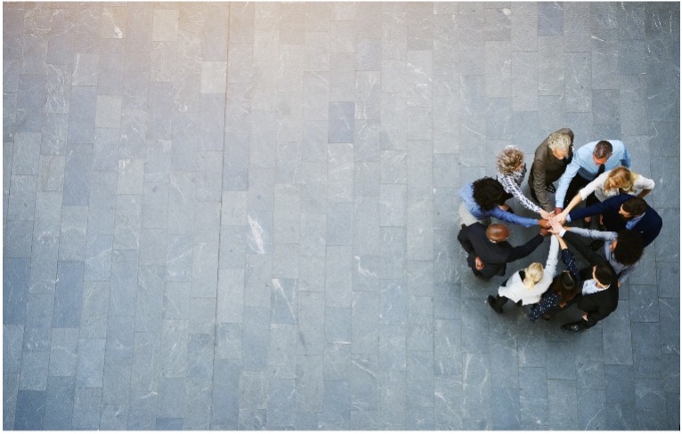 Aerial view of 11 people in a circle with their right hand in the middle